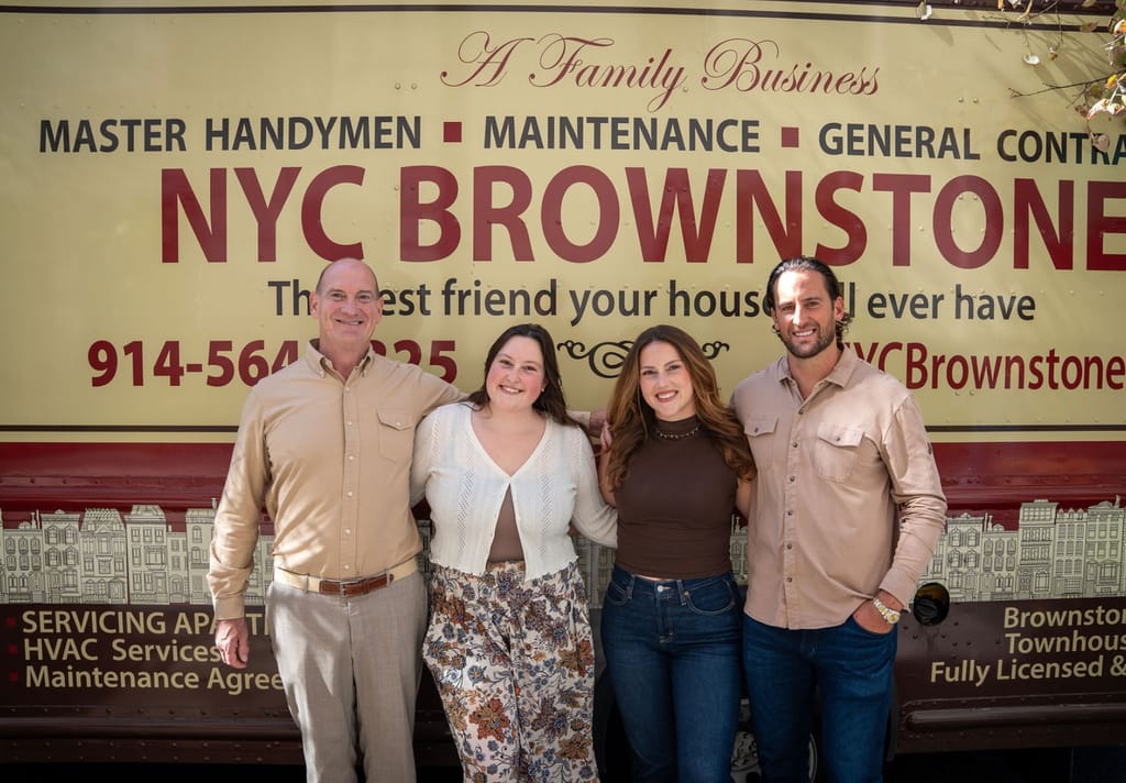 Four of the NYC Brownstone team, two men in tan work shirts and two women, standing arm in arm and smiling in front of one of the company's trucks.